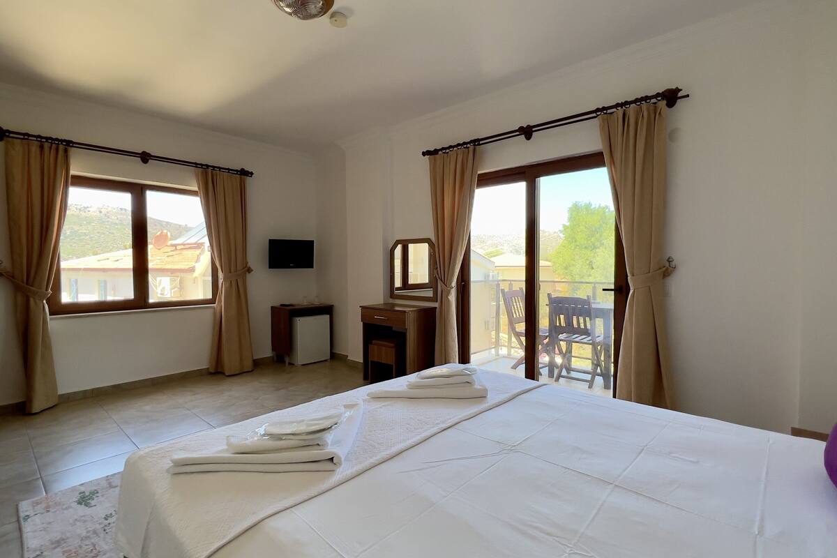 Une chambre d’hôtel avec un lit, un bureau, une télévision et un balcon offrant une vue.