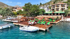 A waterfront restaurant with outdoor seating, a dock with boats, and a hillside backdrop. - Veranda Otel Bozburun (+16) (Marmaris)