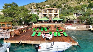 A wooden deck with green lounge chairs and umbrellas, a dining table, and a boat docked nearby.