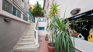 A narrow alley with a staircase leading to a balcony, potted plants, and a tiled wall with a colorful mural. - B&B Antonello (Salerno)