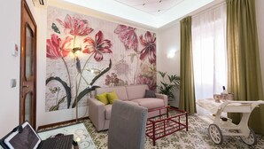 A living room with a floral mural, a sofa, a coffee table with a laptop, and a vintage cart. - B&B Antonello (Salerno)