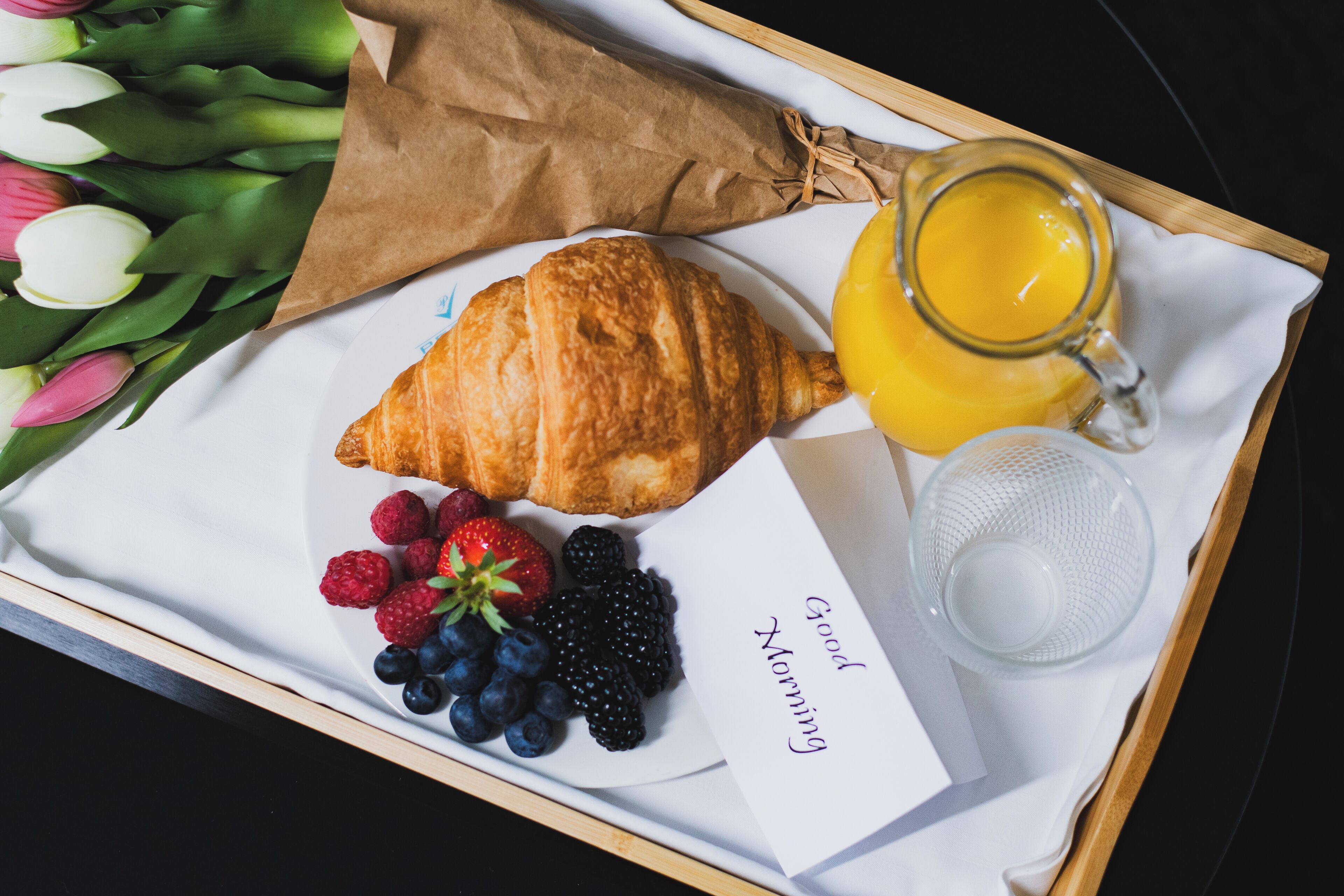 Bandeja de desayuno con croissant, fruta, jugo y una nota que dice 'Buenos días'.
