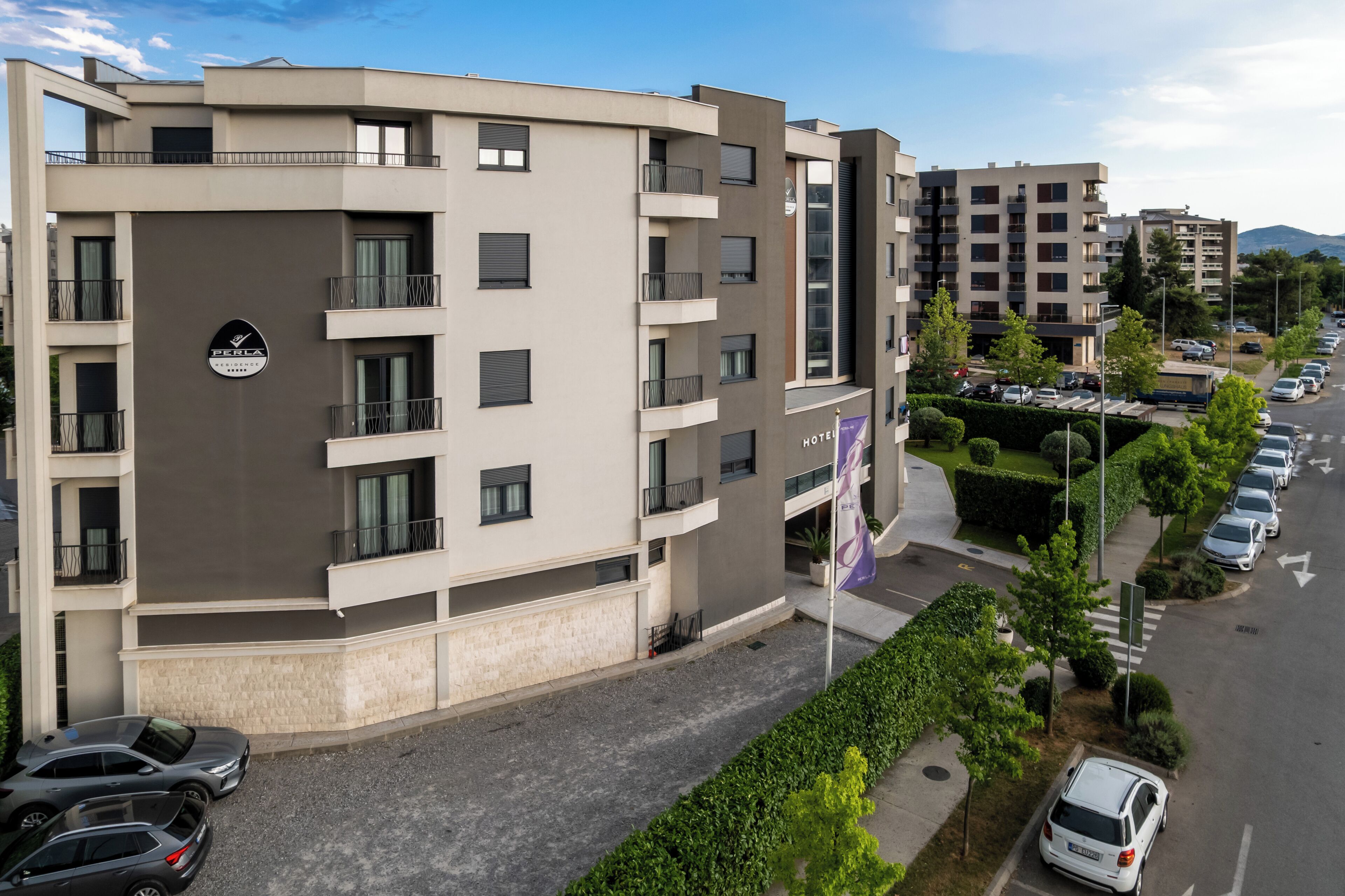 Un hotel moderno de varios pisos con balcones, un área de estacionamiento y una vista despejada de la calle.