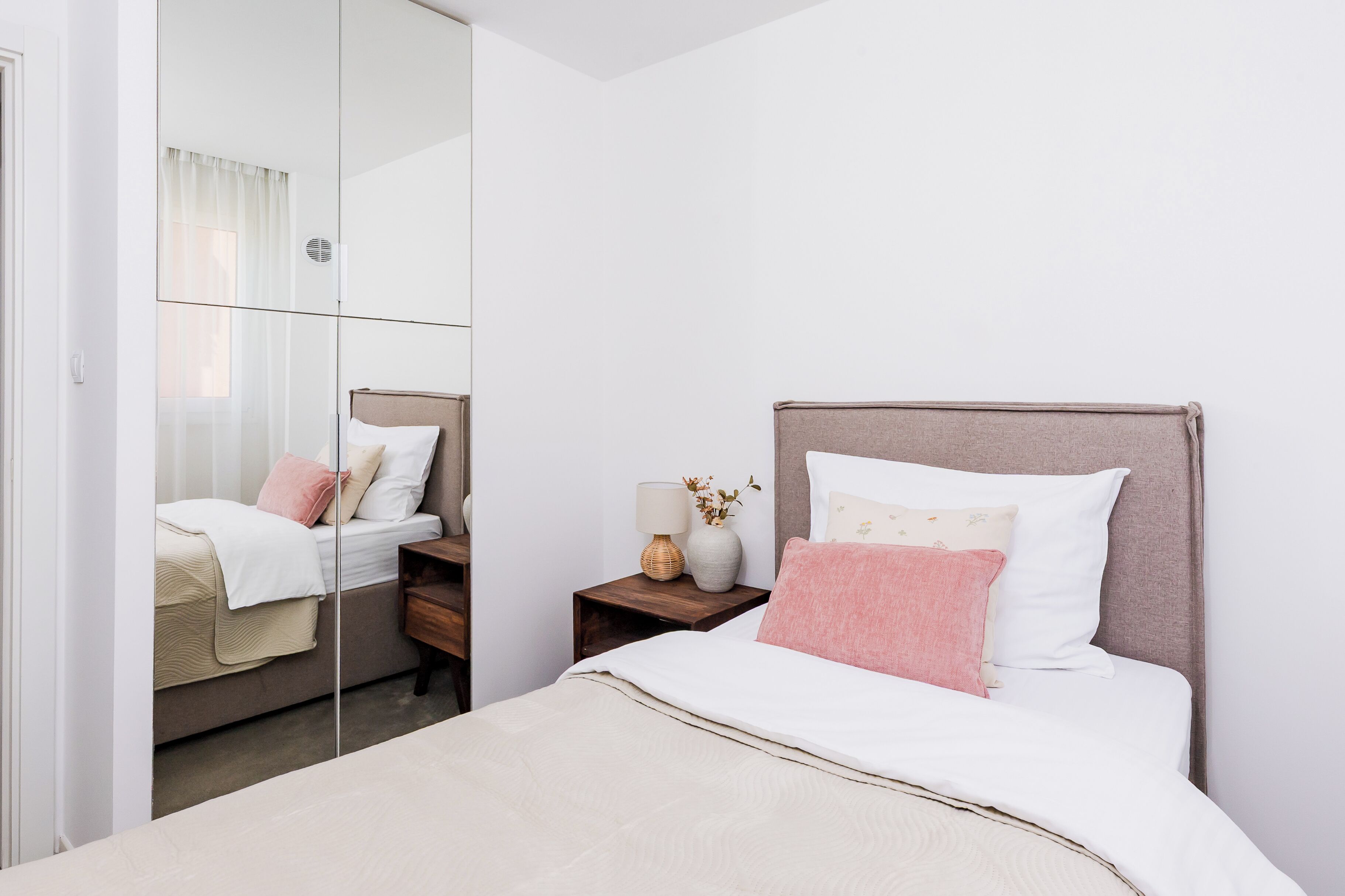 A bedroom with a bed, bedside tables, a mirror, and a window with curtains.