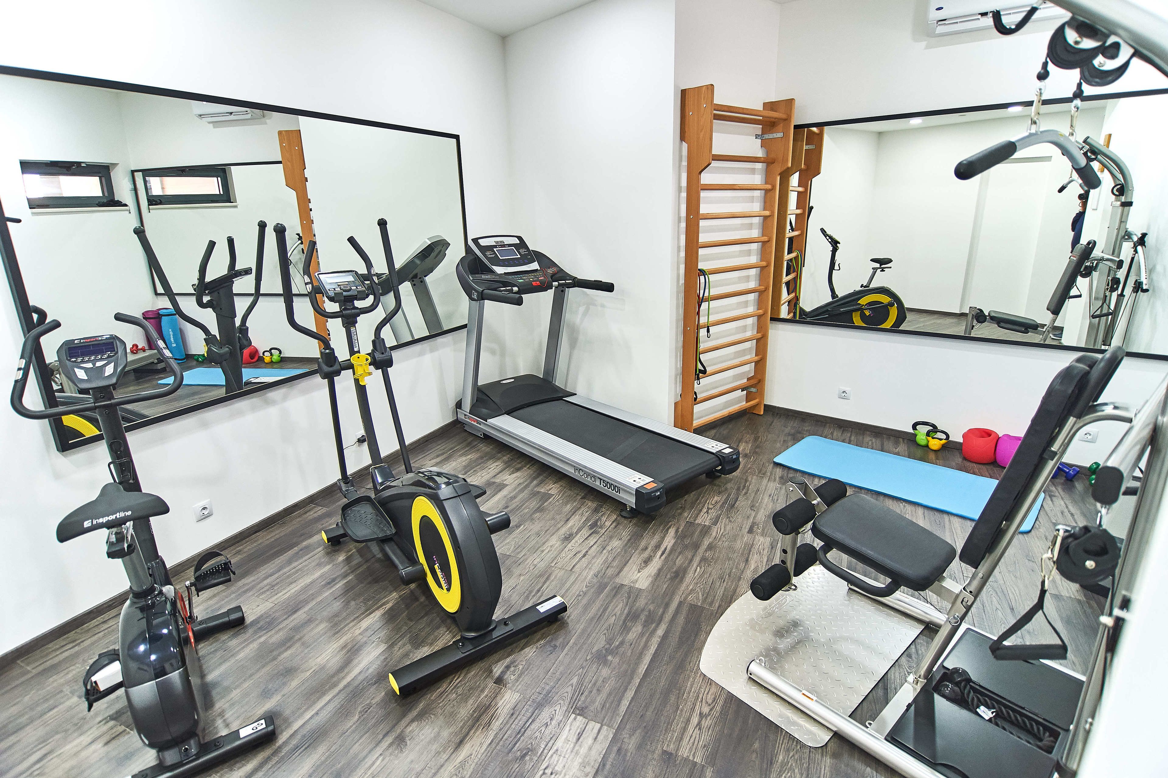 A home gym with a treadmill, stationary bike, elliptical, and weight bench.
