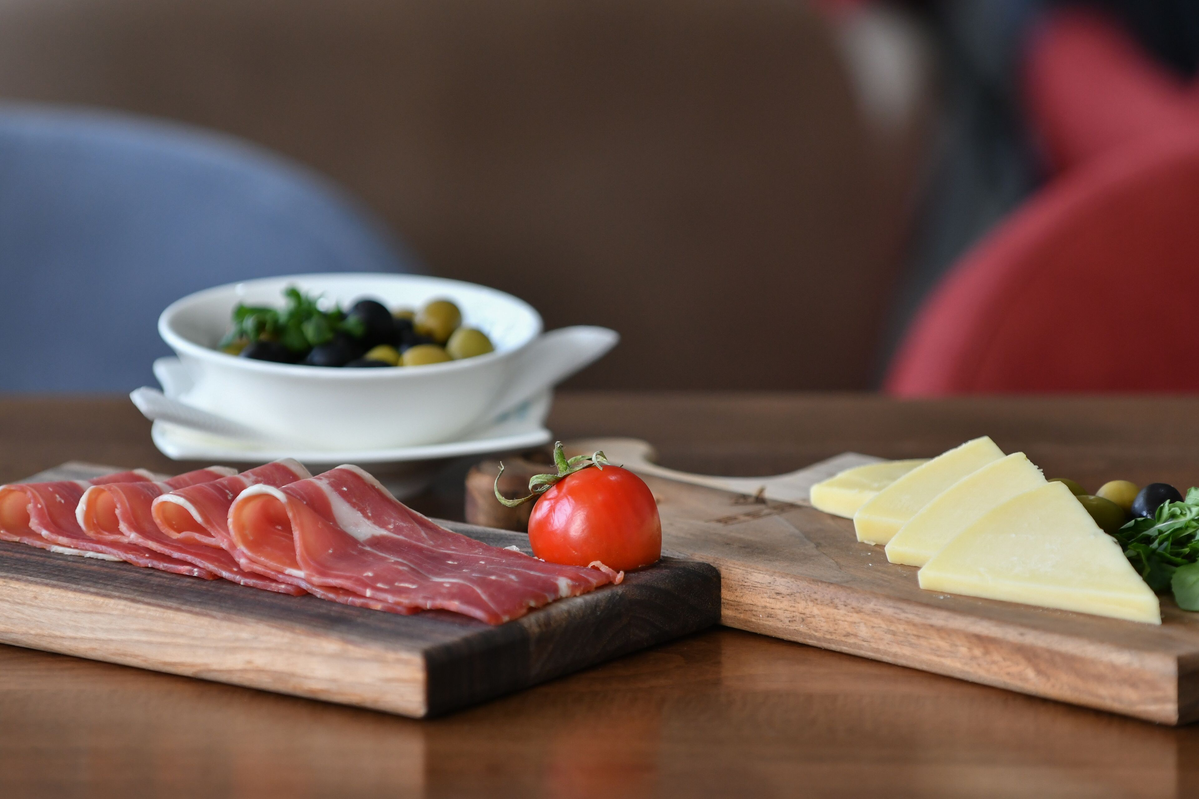 A wooden board with sliced meats, cheese, a tomato, and olives.