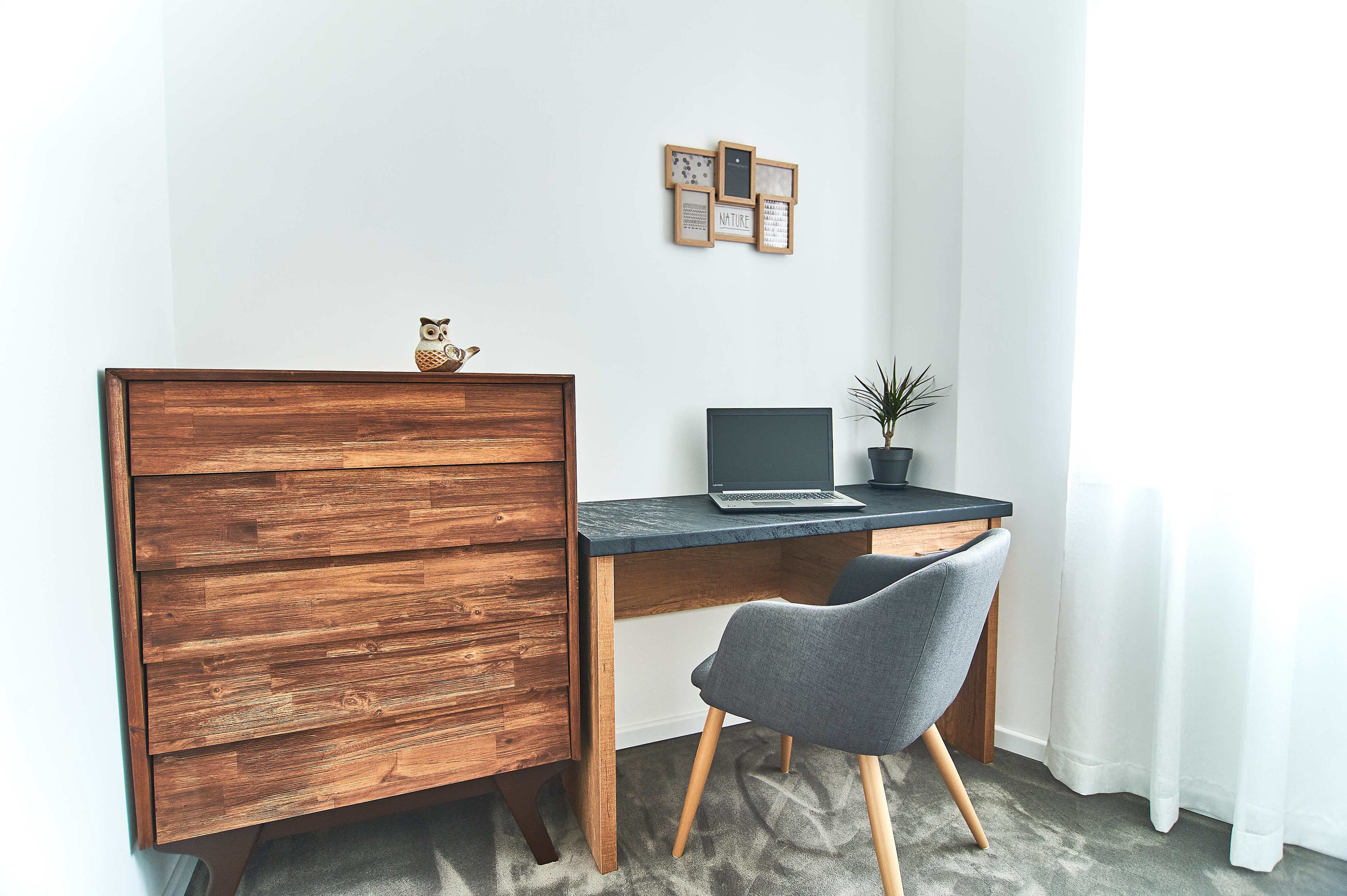 A wooden desk with a laptop, a grey chair, and a small potted plant.