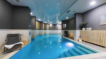 A swimming pool with a clear blue water, surrounded by walls with a modern design, and a wooden fence on one side.
