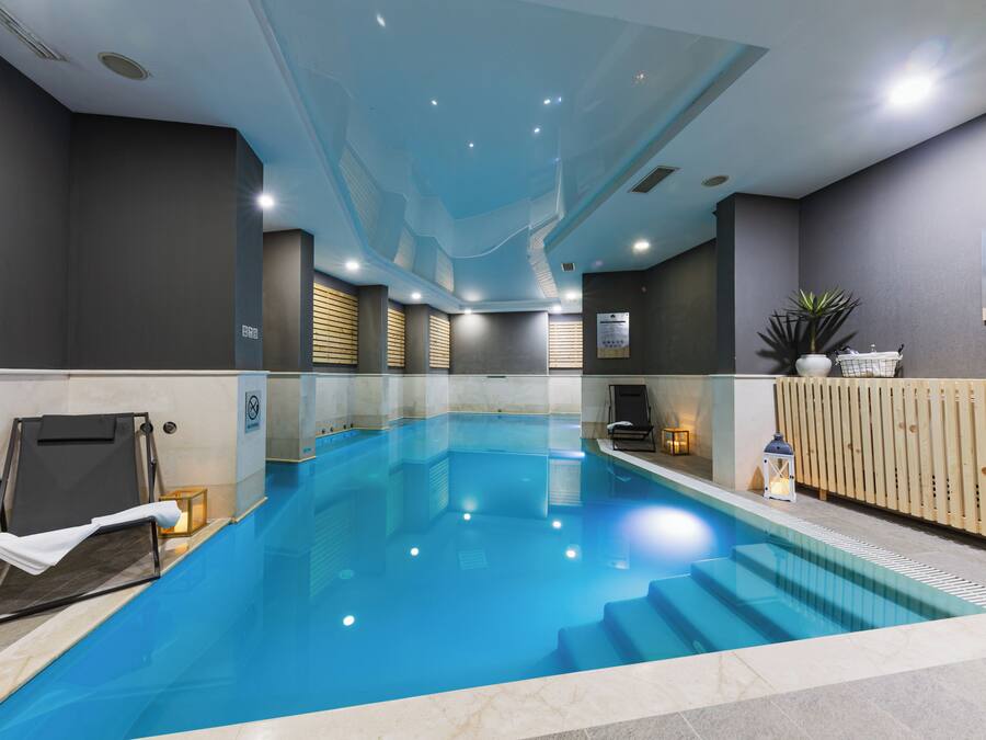 A swimming pool with a clear blue water, surrounded by walls with a modern design, and a wooden fence on one side.