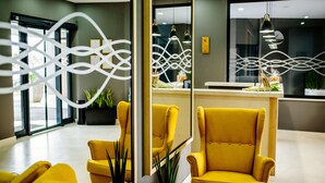 Zona de recepción con diseño moderno, que incluye un sillón amarillo, un mostrador de recepción y una pared decorativa con patrones abstractos.