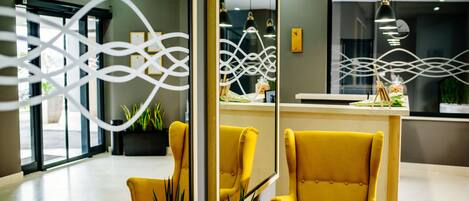 A reception area with a modern design, featuring a yellow armchair, a reception desk, and a decorative wall with abstract patterns.