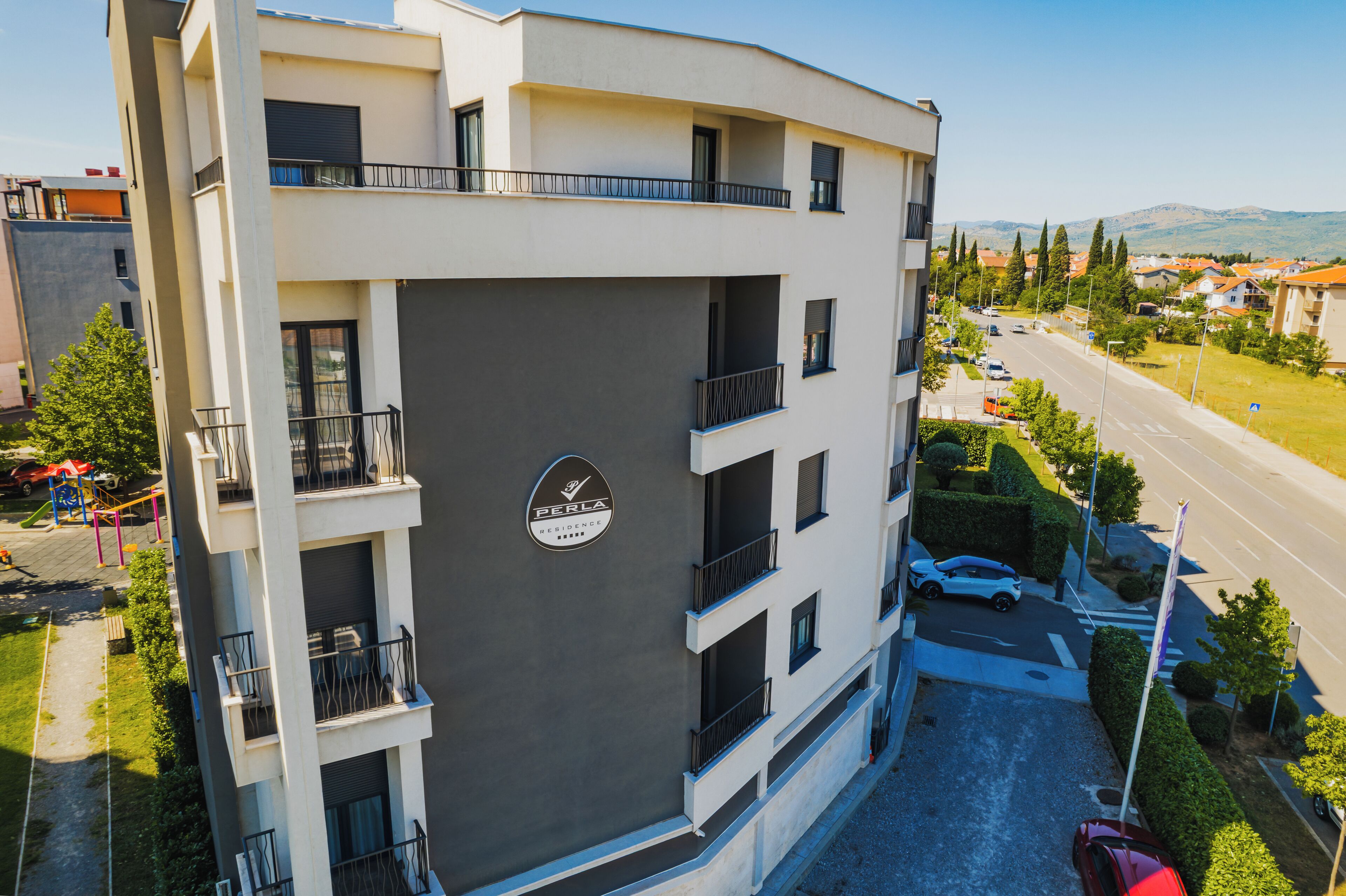 Um edifício residencial com vários andares, varandas, área de estacionamento e vista para a rua e vegetação.