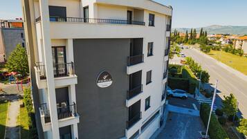 Um edifício residencial com vários andares, varandas, área de estacionamento e vista para a rua e vegetação.