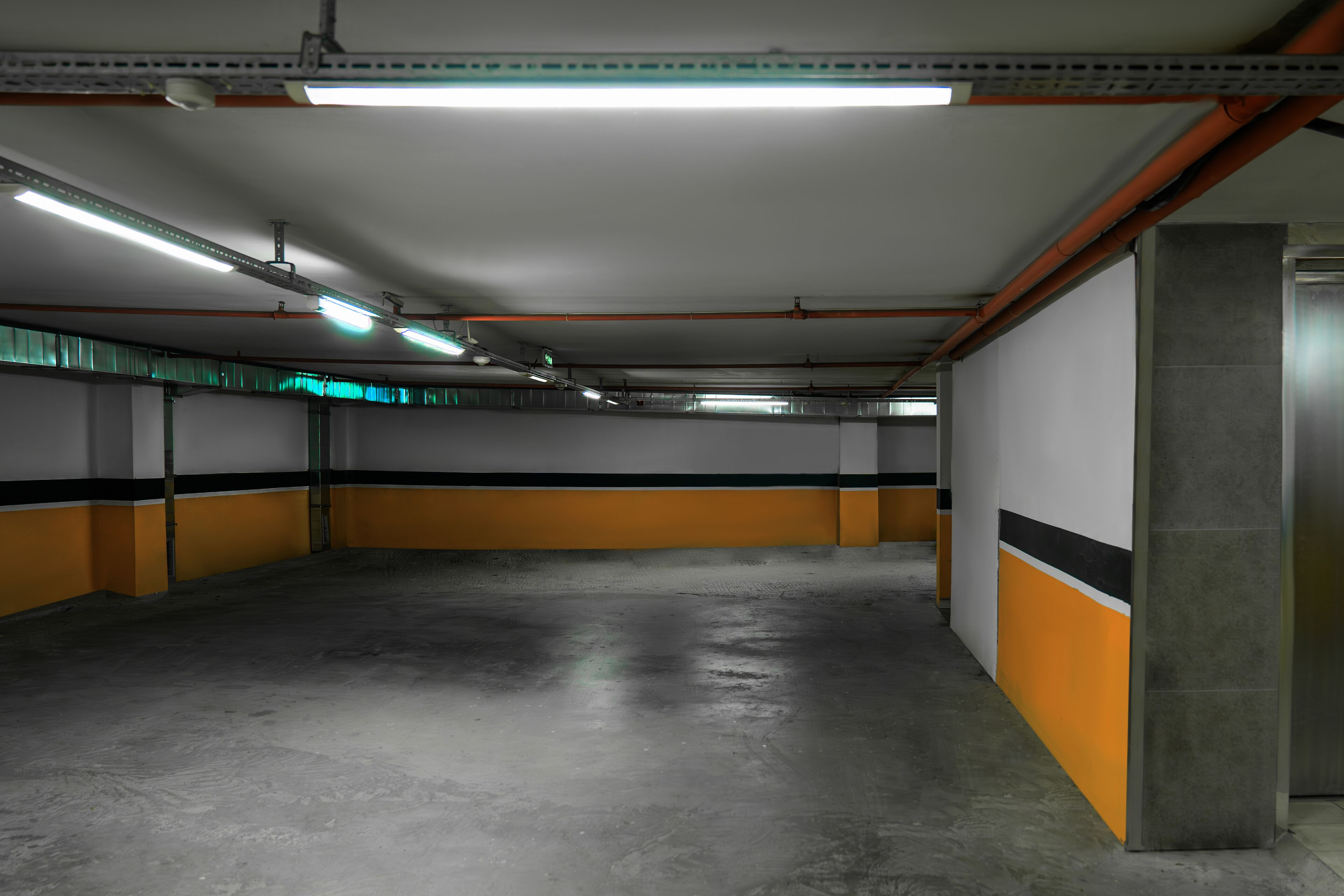 A parking garage with concrete floors, fluorescent lighting, and orange and black walls.