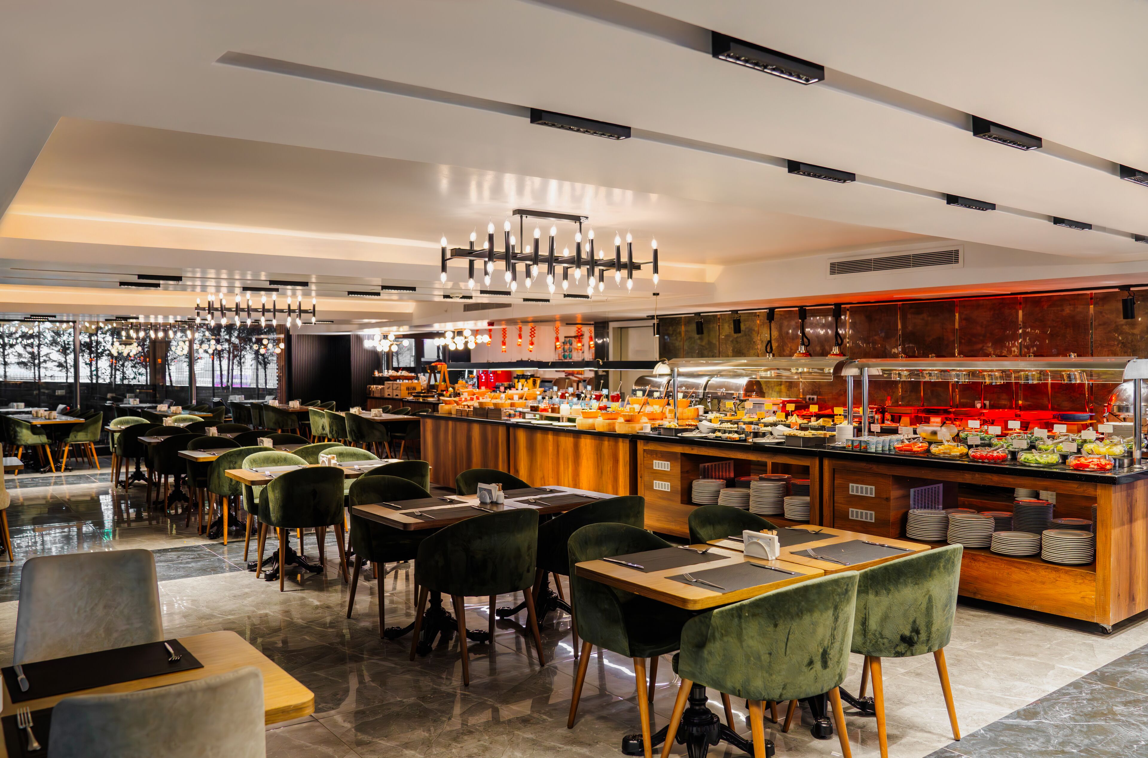 Un restaurante moderno con zona de bufé, sillas tapizadas en verde y diversas opciones de comida.