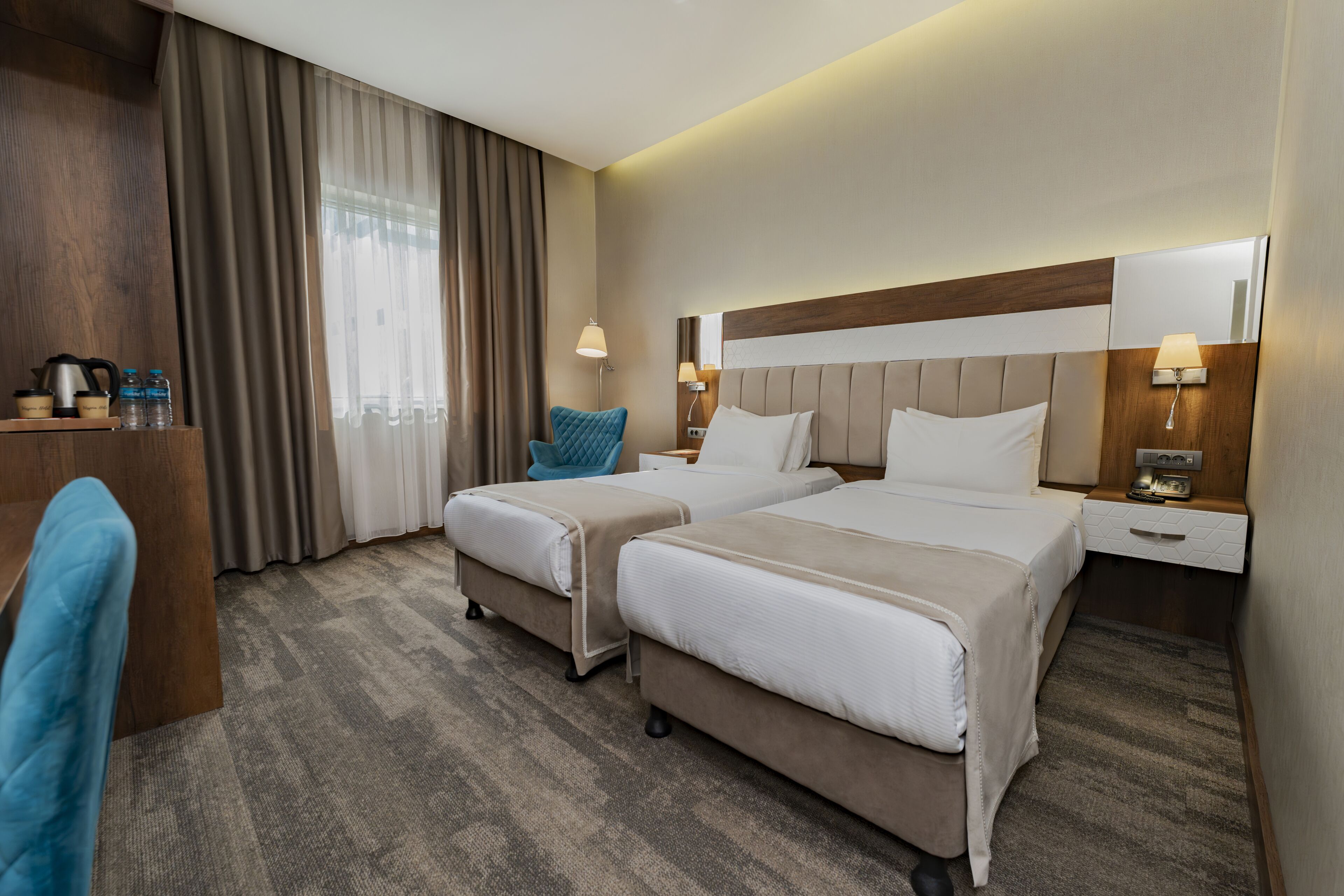 Habitación de hotel con dos camas, un escritorio, una silla y un ventanal con cortinas.