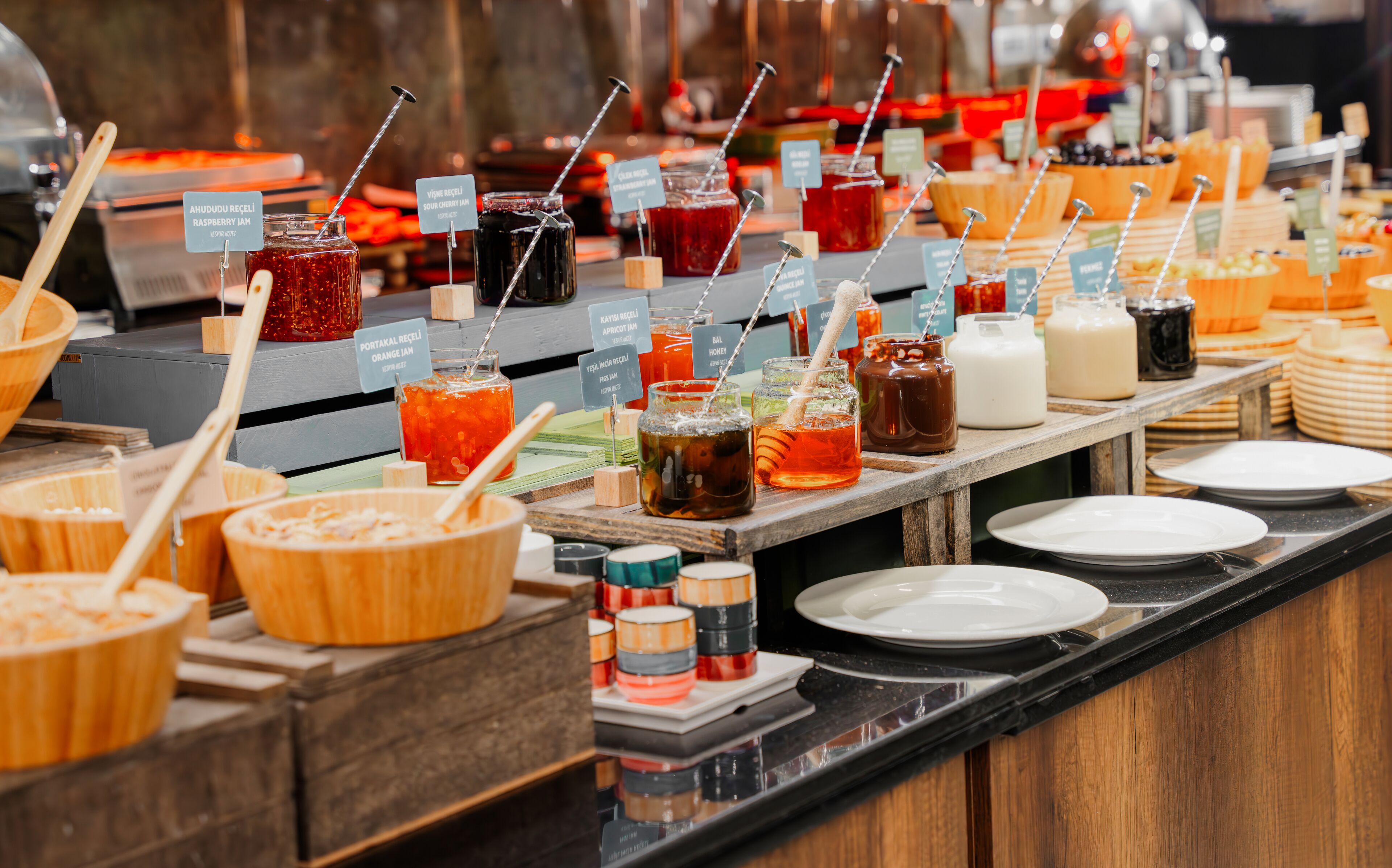 A buffet with various food and drink options, including jars of jams and sauces, and wooden bowls.
