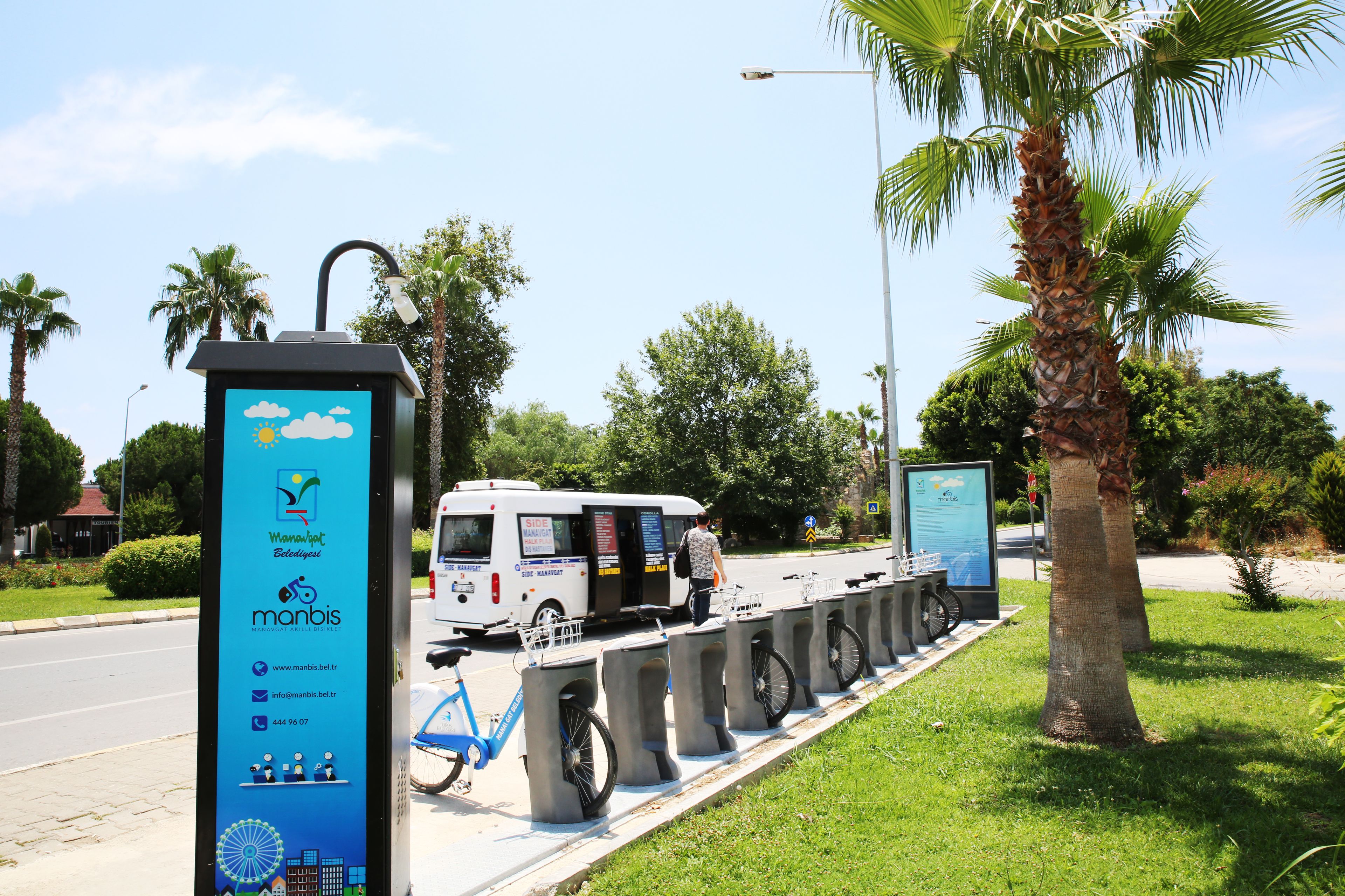 A bus stop with a blue signboard displaying contact information and a bicycle parked nearby.