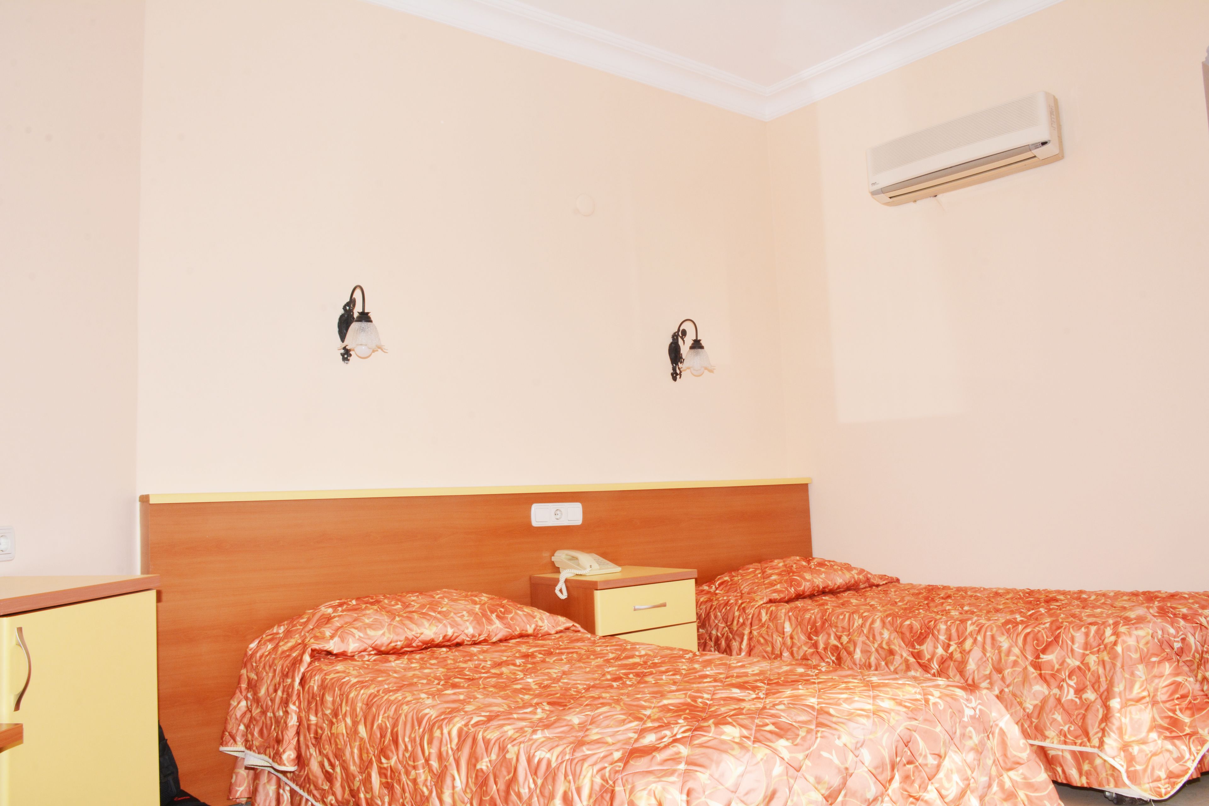 A hotel room with two beds, a wooden headboard, a bedside table with a phone, and an air conditioning unit on the wall.