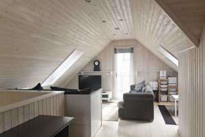A loft-style room with a sloped ceiling, a television, a sofa, and a dining area.