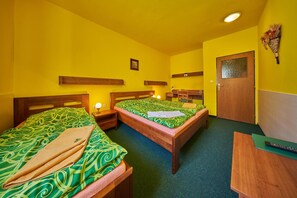 A room with two beds, wooden headboards, a wooden desk, a small table, and a door. - Pension&restaurace Zelený Mlýn (Zacler)