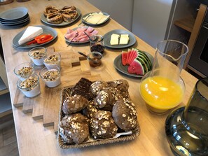 A breakfast table with various food items including bread, cheese, ham, and fruit. - Birkelygaard Bed & Breakfast (Millinge)