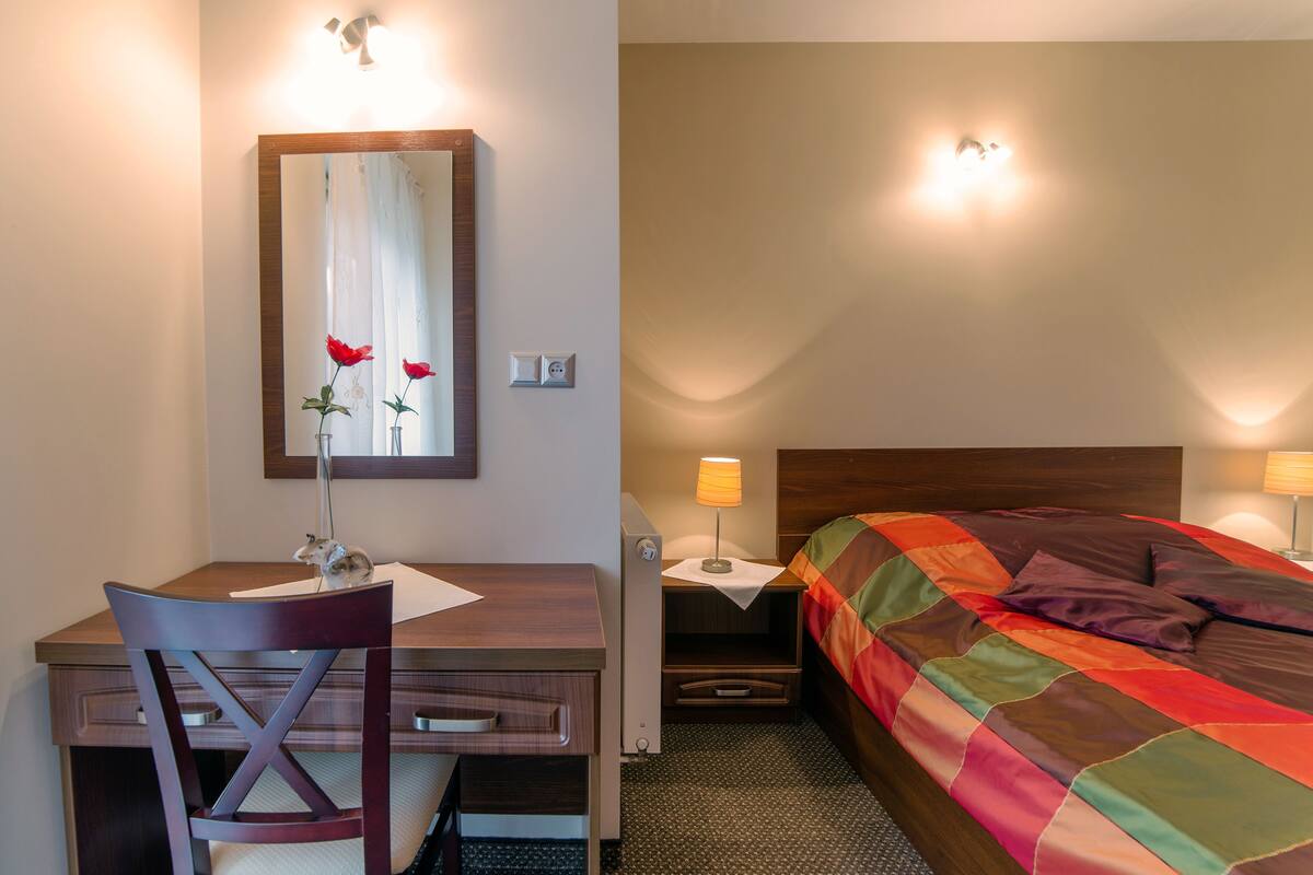 A hotel room with a wooden desk, a chair, a bed with a colorful quilt, and bedside lamps.