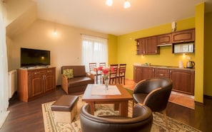 Una sala de estar con un sofá, una mesa de centro y un televisor. Hay un comedor con una mesa y sillas. La cocina tiene armarios de madera y una estufa.