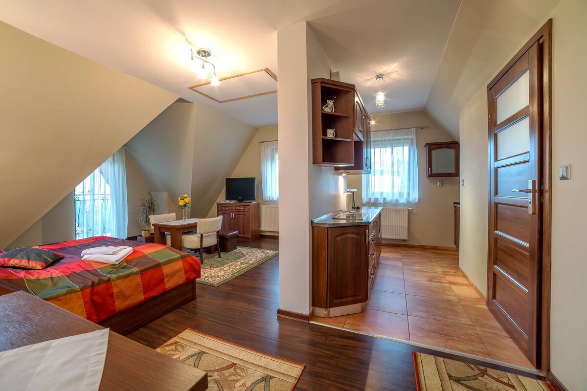 A bedroom with a bed, a desk, a chair, and a kitchenette.