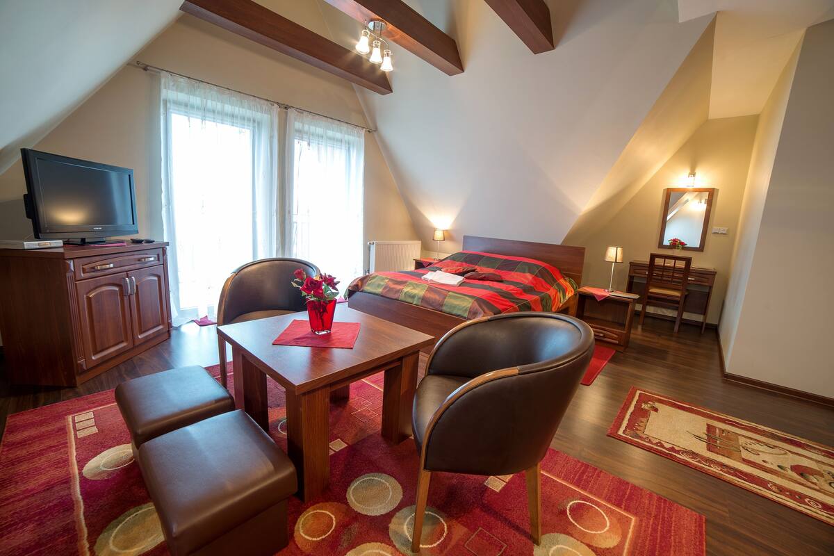 A bedroom with a bed, a desk, a chair, a television, and a window.