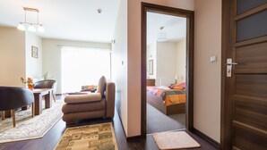 Ein modernes Hotelzimmer mit Holzboden, einer Couch, einem Esstisch und Blick in das angrenzende Schlafzimmer.