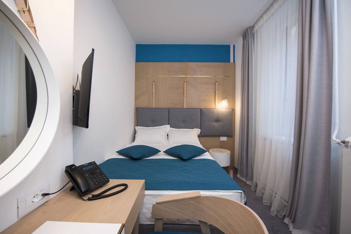 Habitación de hotel con cama, escritorio con teléfono, televisor de pared y lámpara de noche.