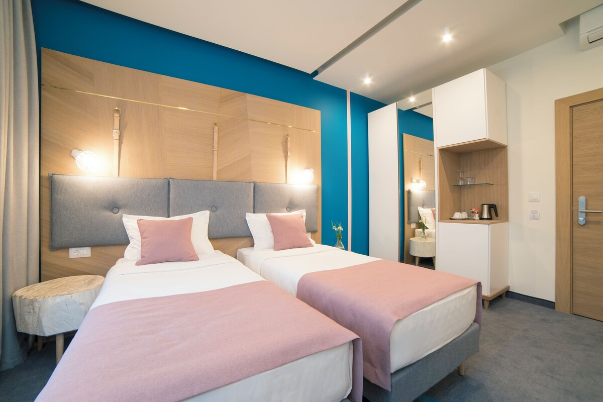 Ein Hotelzimmer mit zwei Betten, einem kleinen runden Tisch, einem Spiegel und einer Küchenzeile.