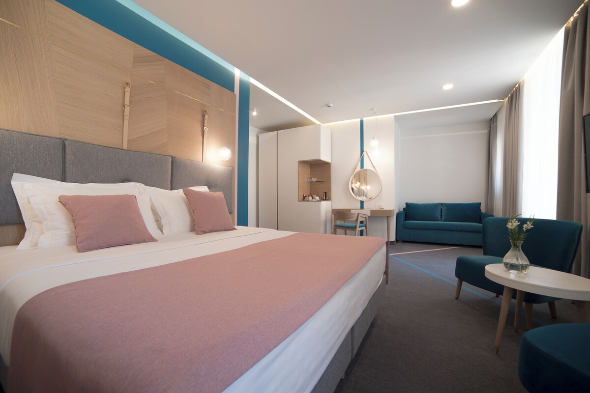 Ein modernes Hotelzimmer mit einem großen Bett, einem Schreibtisch, einer Couch und einem kleinen Tisch mit einer Vase.