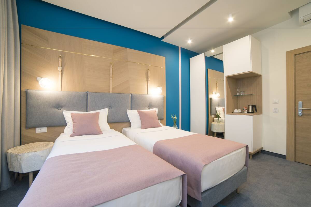 Habitación de hotel con dos camas, una mesita redonda pequeña, un espejo y una zona de kitchenette.