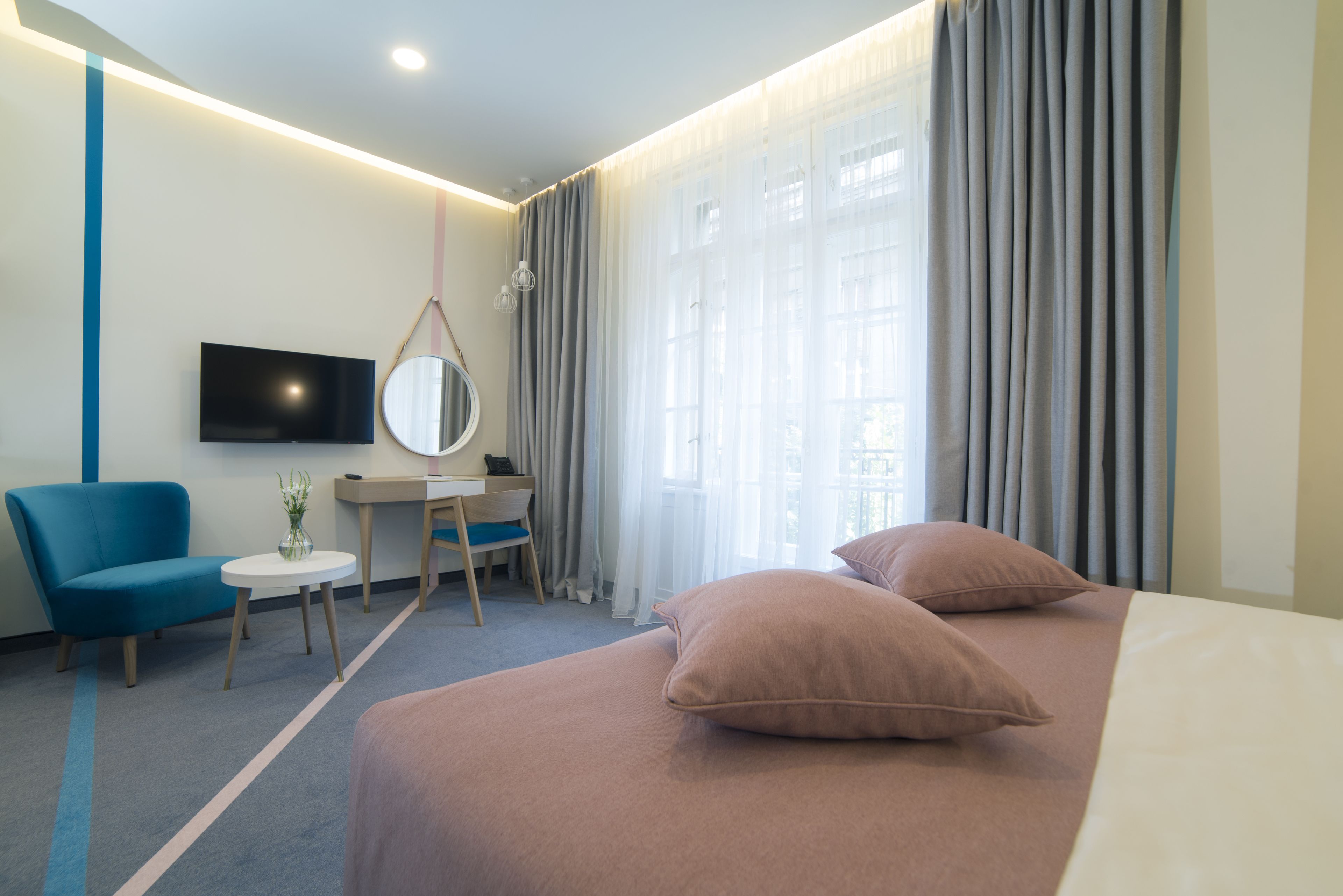 A hotel room with a bed, a desk, a chair, a TV, and a window with curtains.