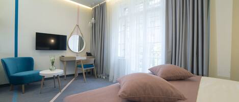 A hotel room with a bed, a desk, a chair, a TV, and a window with curtains.
