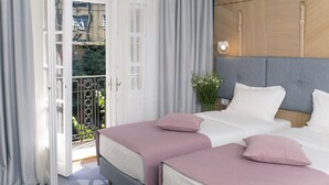 A hotel room with a balcony, a bed with white bedding and pink pillows, and a grey headboard. - City Nest Modern & Cozy Suites (Belgrade)