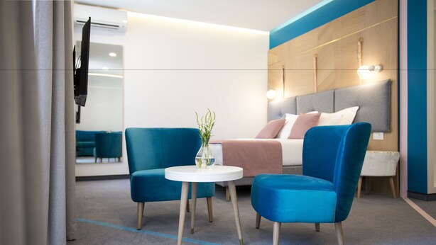 A modern hotel room with a bed, two blue armchairs, a small white table, and a mirror. - City Nest Modern & Cozy Suites (Belgrade)