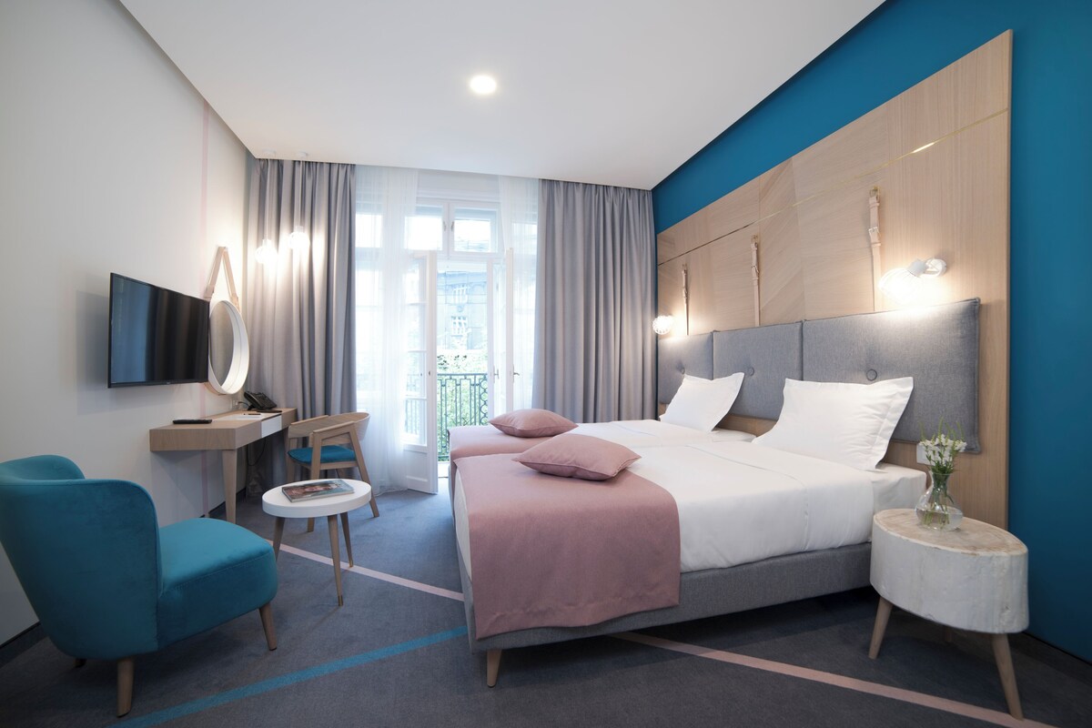 Ein modernes Hotelzimmer mit Bett, Schreibtisch, Stuhl, Fernseher und Blick ins Freie.