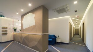 A reception area with a modern design, including a reception desk, a blue sofa, and a small side table with a plant. - City Nest Modern & Cozy Suites (Belgrade)