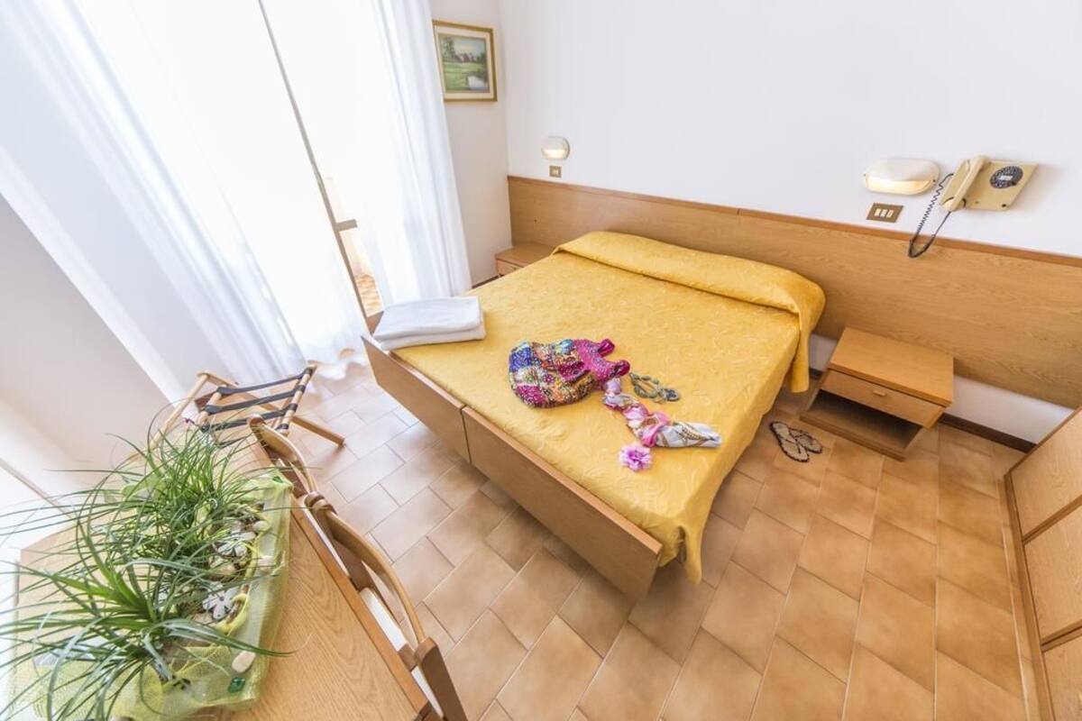 Une chambre d’hôtel avec un lit, une table de chevet, un petit bureau avec une chaise, une plante en pot et un téléphone fixé au mur.