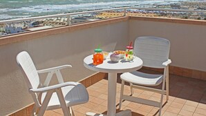 Een balkon met twee witte stoelen en een kleine tafel, met uitzicht op een strand met parasols en het ocean.