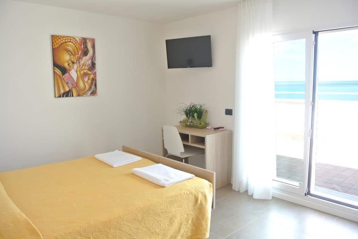 Une chambre d’hôtel avec un lit, un bureau, une télévision et une vue sur la mer.