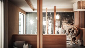 A modern interior with a wooden bench, large windows, and a rustic wooden machine. - Hotel Gasserhof Tradition & Lifestyle (Bressanone)