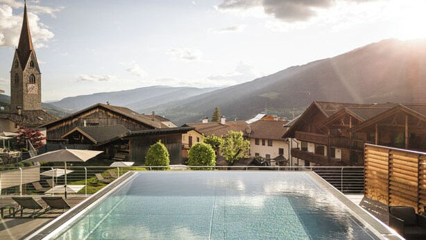 A swimming pool with a view of traditional buildings and a church. - Hotel Gasserhof Tradition & Lifestyle (Bressanone)