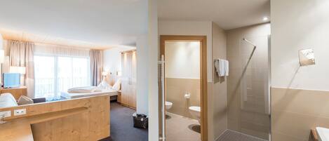 A modern hotel room with a wooden desk, a bed, a bathroom with a shower, and a toilet.