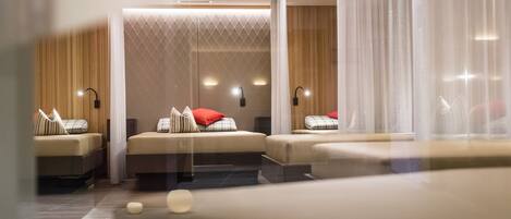 A modern hotel room with a large bed, two smaller beds, and a seating area.