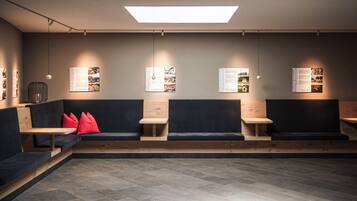 A modern waiting area with a central seating area, wooden tables, and informational posters on the walls.