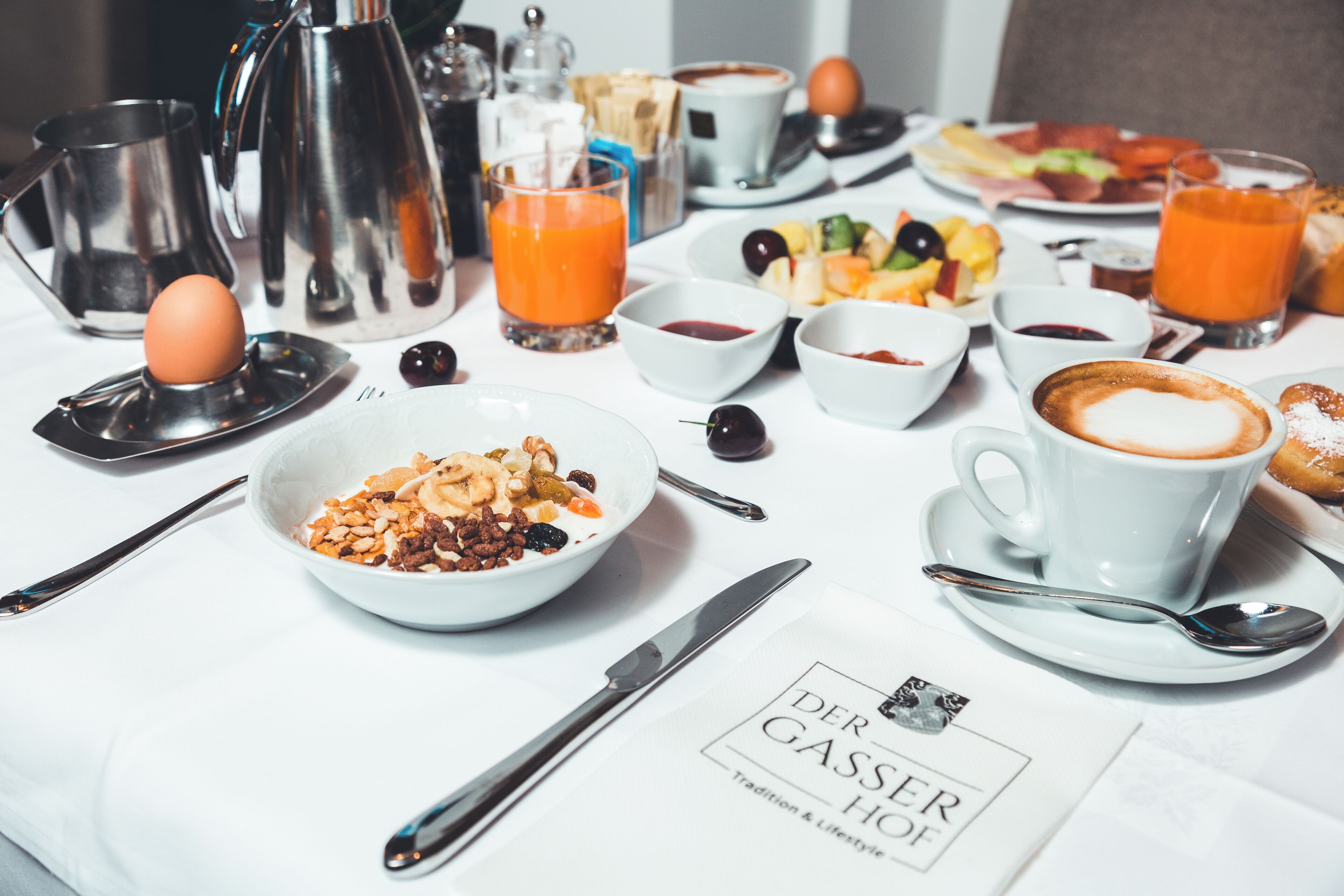 A breakfast setting with various dishes, a coffee cup, and a teapot on a table.